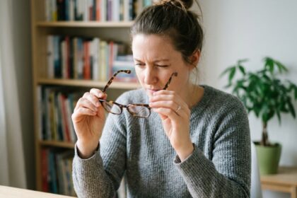 Femme examinant des lunettes achetées en ligne avant le Black Friday, assise à un bureau en bois dans un espace de travail moderne