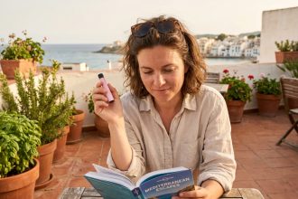 Femme en vacances tenant une puff sur une terrasse méditerranéenne avec un guide de voyage ouvert