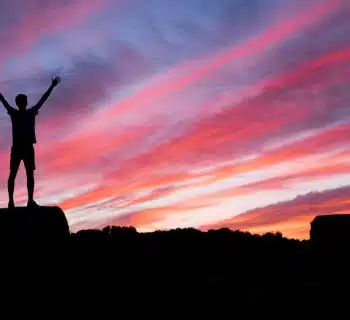 silhouette of man standing on high ground under red and blue skies